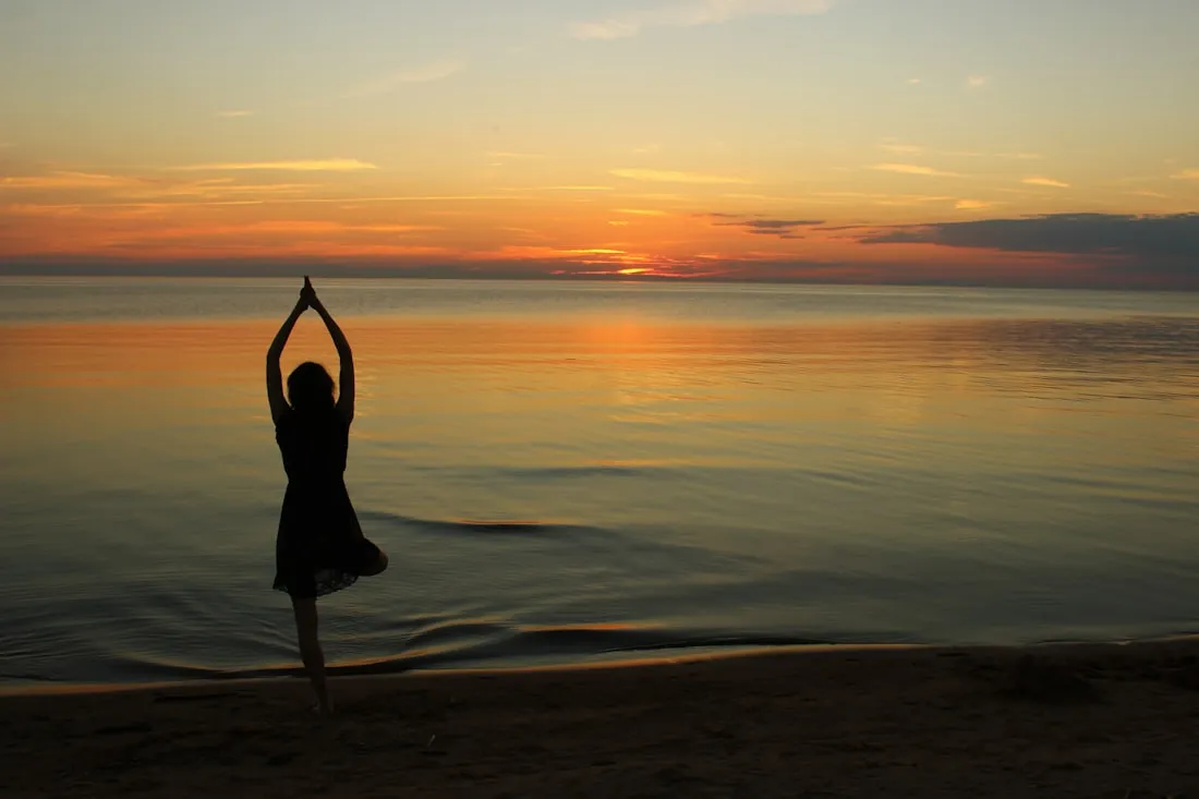 A figure in tree pose against a golden sunset by the water